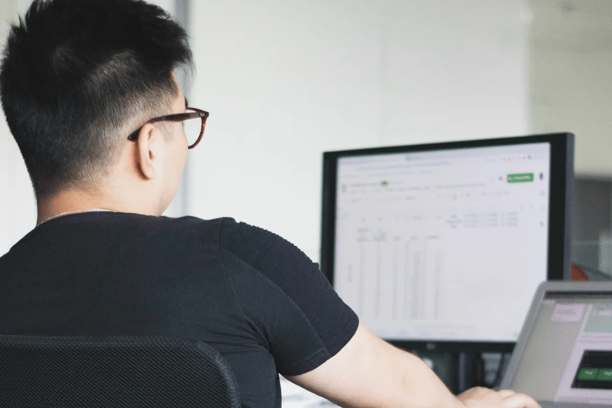 Office worker analyzing financial or performance data in a spreadsheet displayed on a desktop monitor.