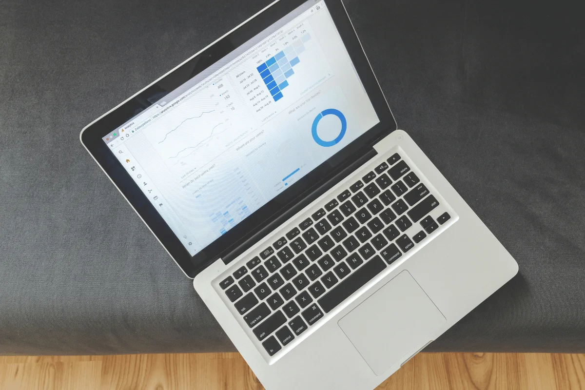 Open laptop on a dark sofa displays analytical graphs and a blue pie chart, conveying a professional, data-focused atmosphere.